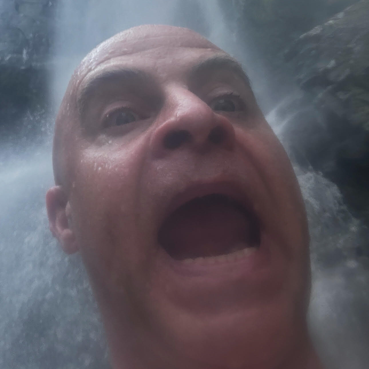 Bald man with funny expression under waterfall